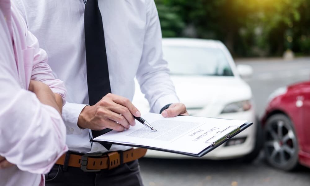 Insurance agent inspecting a vehicle and taking notes on a clipboard while assessing and processing a car accident claim.