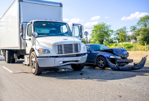 A large white semi-truck involved in a collision with a black car on a road, showing significant front-end damage to the car.