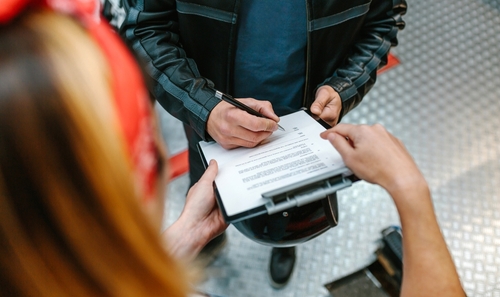 A person signing a document on a clipboard held by another individual, suggesting an agreement or legal paperwork related to a motorcycle case.