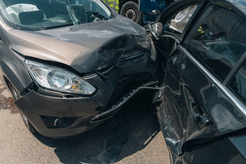 A close-up of two heavily damaged cars after a collision, showing crumpled fronts and broken glass on a street.