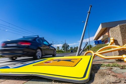 A black car speeding away past a fallen traffic sign and damaged light pole, indicating the aftermath of a hit-and-run collision.