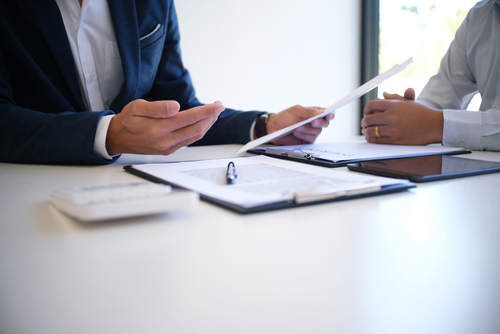 Two individuals seated at a table in a professional setting, reviewing legal documents together, with one person gesturing while the other listens attentively.