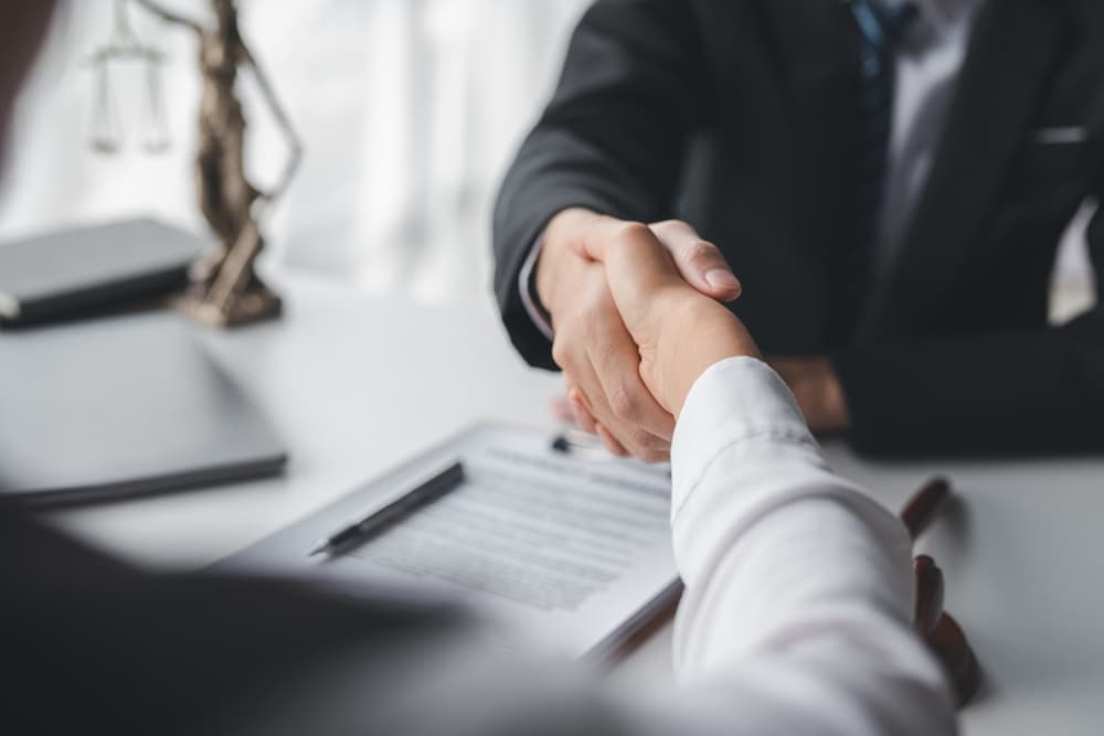 Lawyer shaking hands with a client making about documents, contracts, agreements, cooperation agreements with a female client at the lawyer's desk and a hammer at the table.