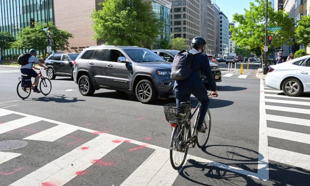 Group of cyclists navigating through traffic at a busy intersection in downtown Washington, D.C., during their commute to work.