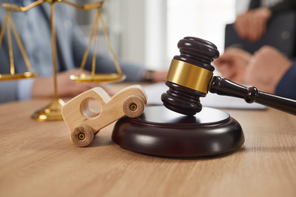 Wooden toy car next to judge’s gavel and legal scales symbolizing a lawyer’s role in helping clients seek justice and compensation after a car accident.