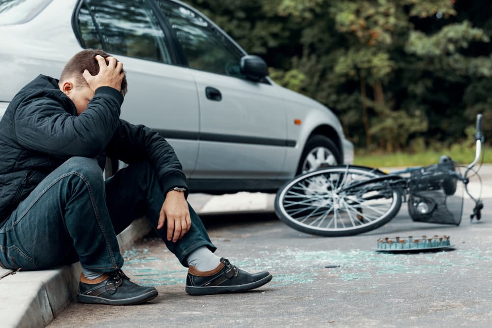 Injured cyclist sitting on the ground holding his head after a bicycle accident with a car, showing head injury risk and the need for legal help.