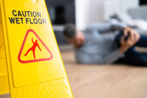Yellow wet floor sign with injured person in background, illustrating a slip and fall accident in Bellevue WA
