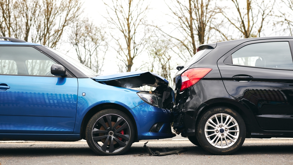 Two cars involved in a rear-end collision at a roadway, showing significant damage