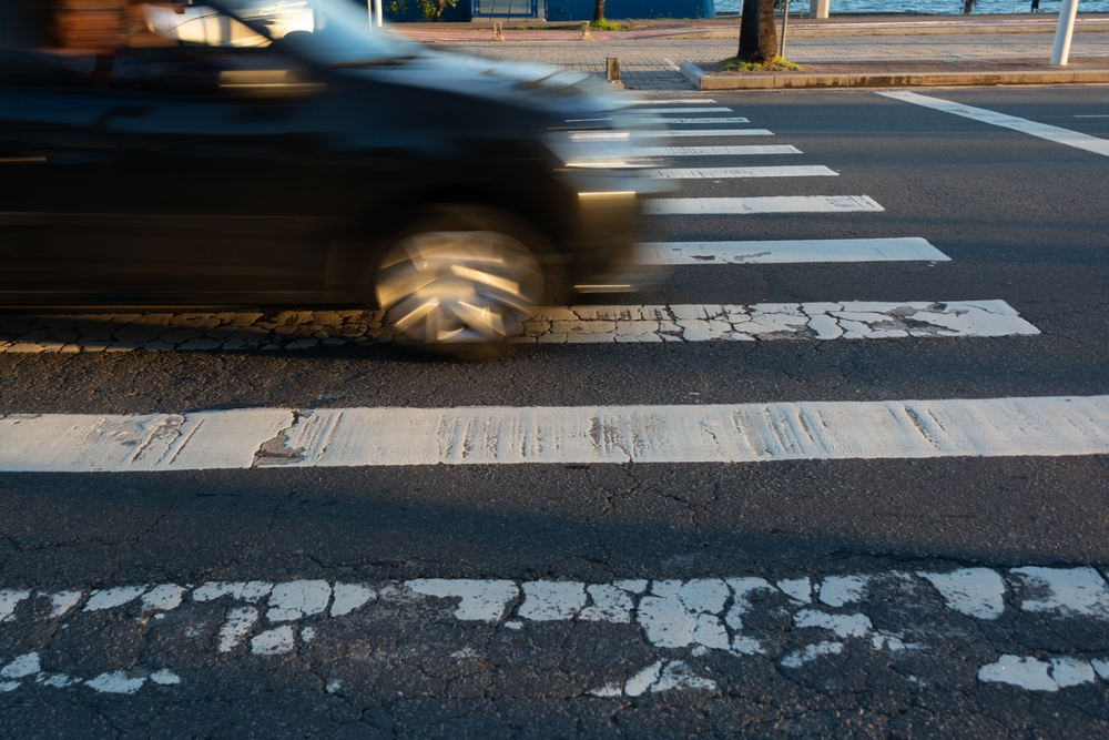 Car speeding through a marked crosswalk, endangering pedestrians and showing reckless driving behavior.