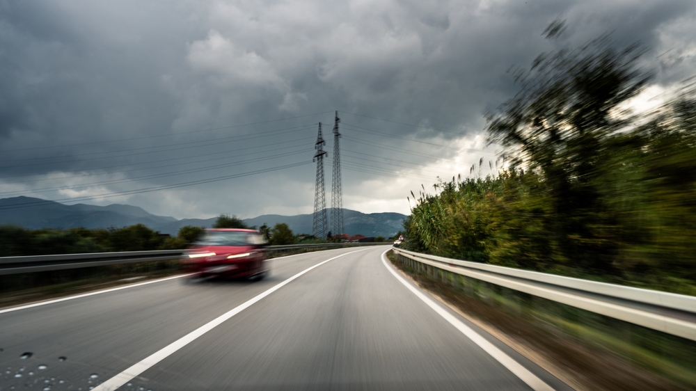 Red car speeding on a Washington highway during stormy weather, illustrating reckless driving