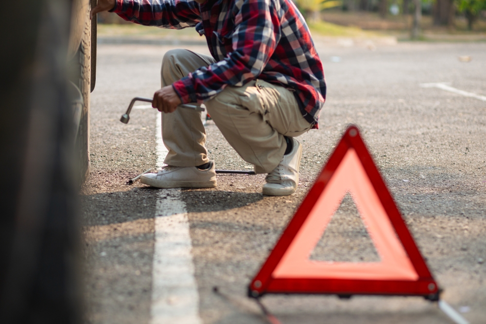 도로 위험 요소(예: 파편이나 움푹 패인 곳)에 부딪힌 후 도로변에서 펑크난 타이어를 고치는 운전자