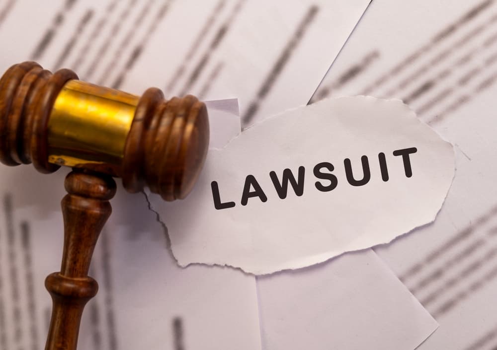 Wooden gavel and torn paper with "Lawsuit" text. Legal action