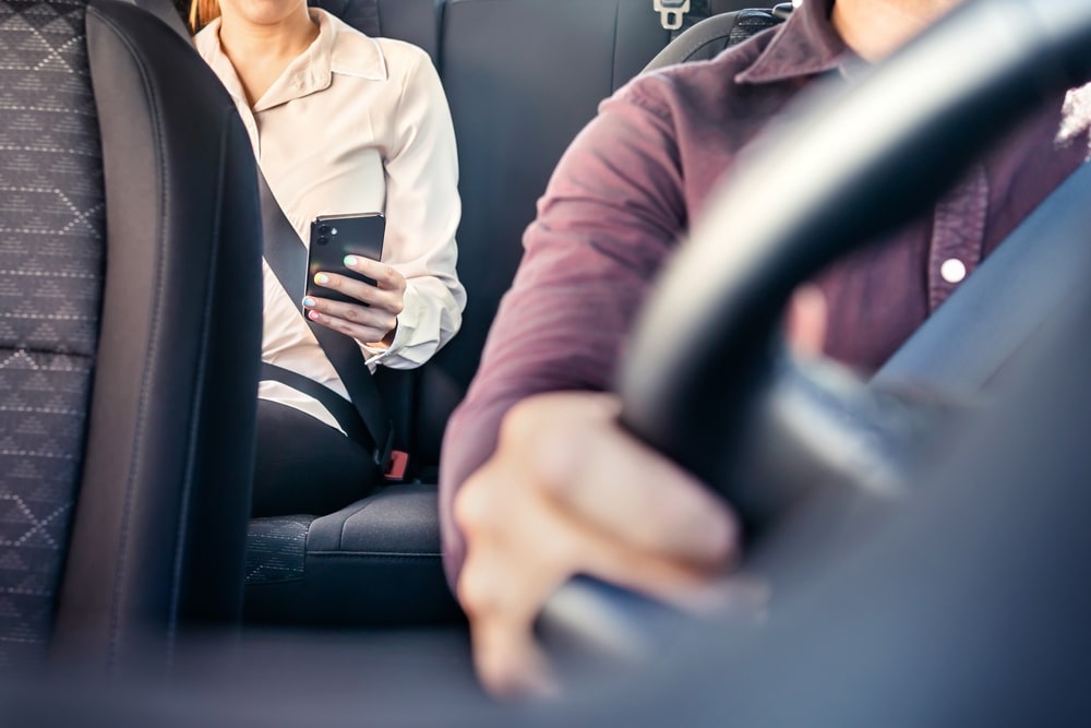 Rideshare passenger seated in the back seat while using a smartphone